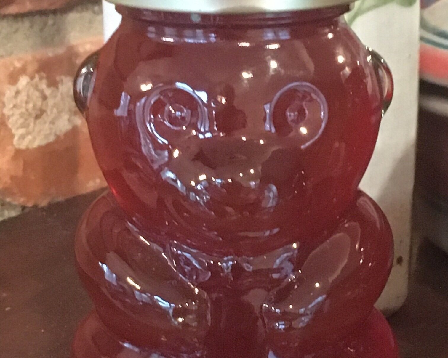 Close-up of a honey jar shaped like a bear, filled with amber-colored honey, resting on a wooden surface with a rustic background.