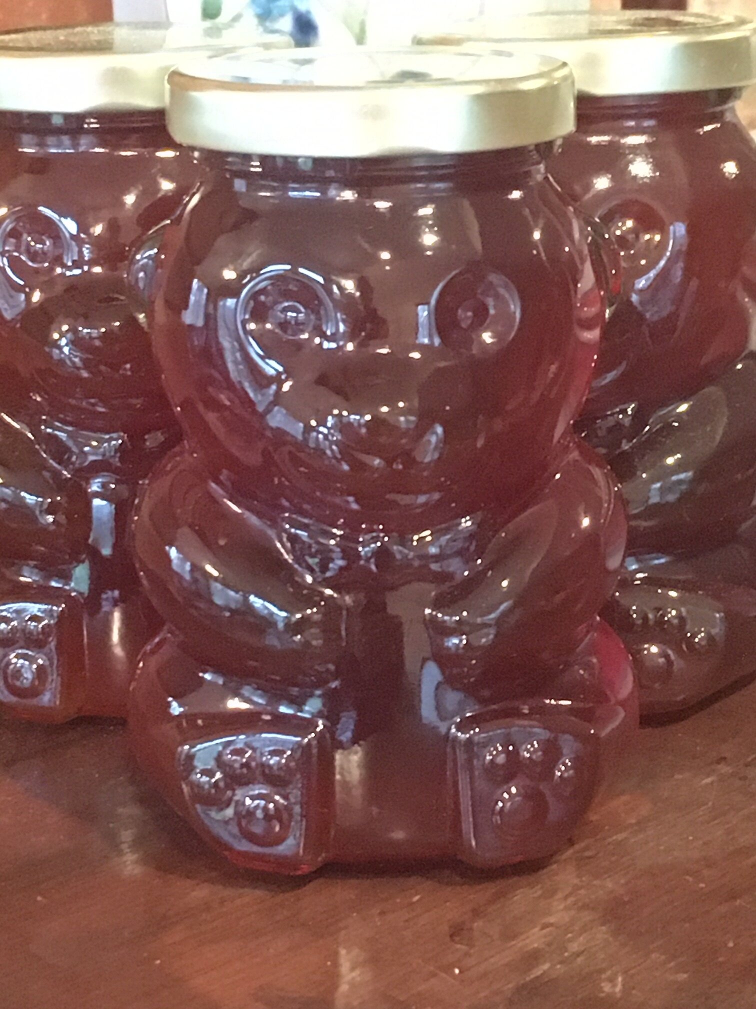 Close-up of bear-shaped jars filled with honey, featuring a shiny exterior and gold lids, arranged on a wooden surface.